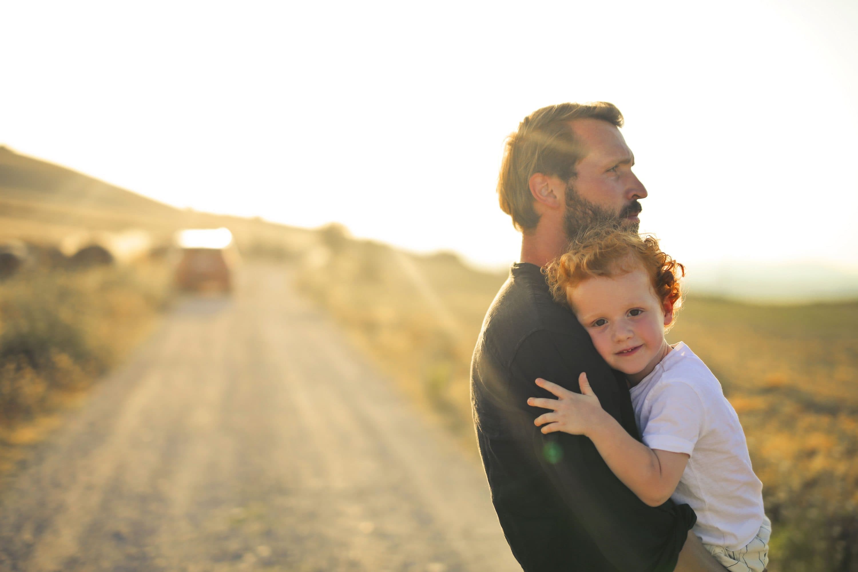 A father holding his young son on a sunlit country road
